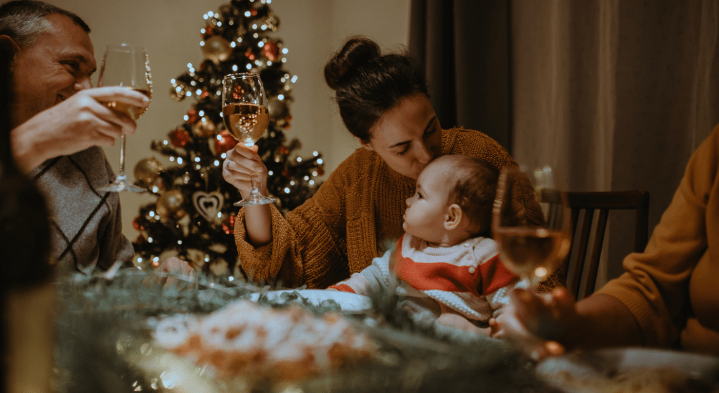 woman raising a glass of wine to toast with family at Christmas while kissing her baby's forehead