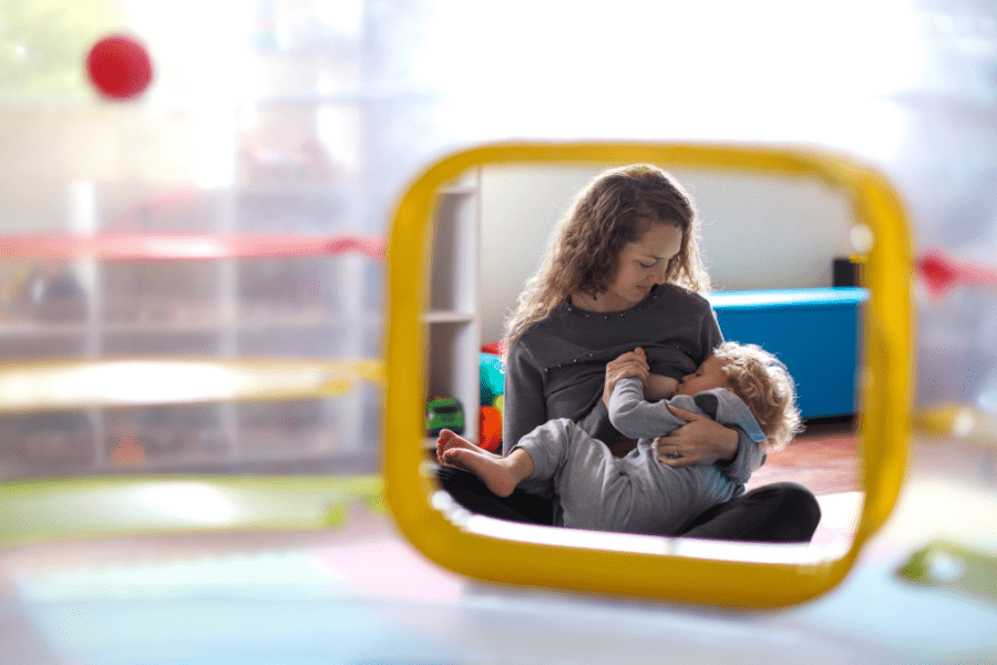 Mother breastfeeds toddler son in a playroom.