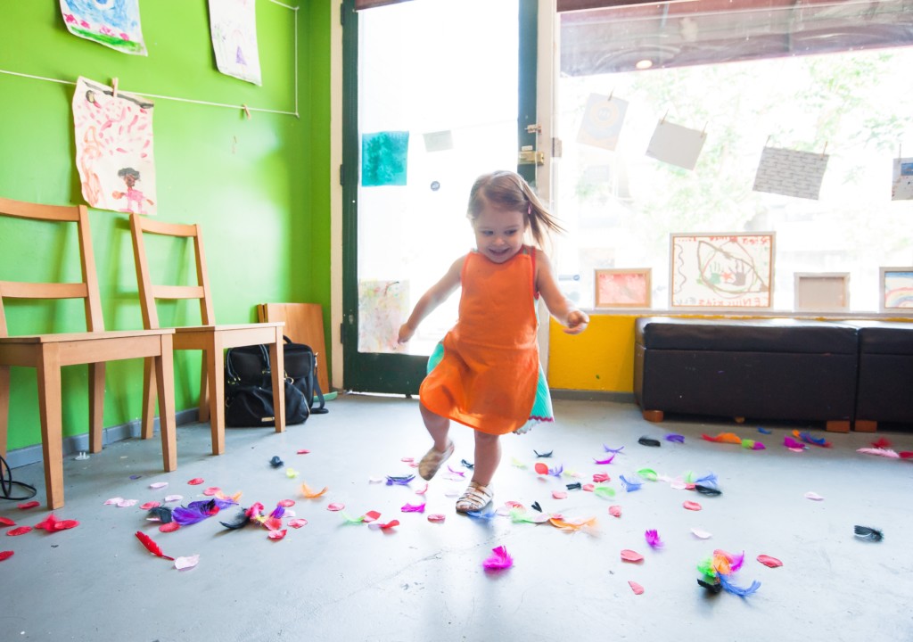 A girl plays and dances with scrap pieces of paper on the floor.