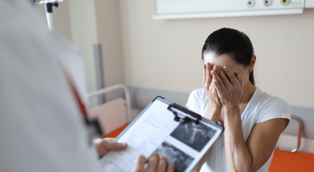 A sad mother holds her face in her hands while doctor tells her of her pregnancy loss.