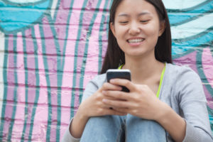 teen texting smile graffiti wall sitting
