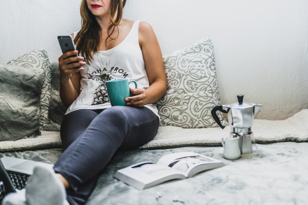 woman on a bed with coffee and a phone and a book