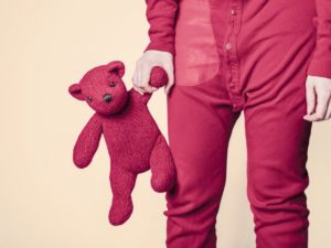 child standing in pajamas holding a teddy bear