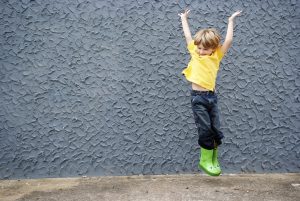 A young boy jumps in a pair of bright green frog rain boots.
