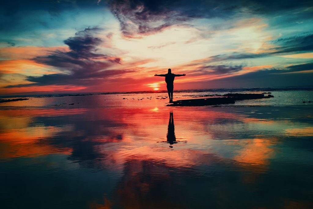 vibrant beach sunset with silhouette of a person with arms outstretched