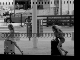 Two girls running through the airport with their suitcases.