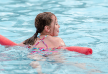 A young girl floats on a noodle in a pool.