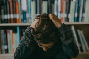 A person bows their head in frustration in a library.
