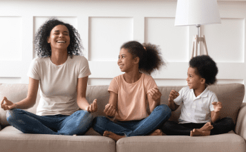 A mom and her kids sit on the couch to meditate.