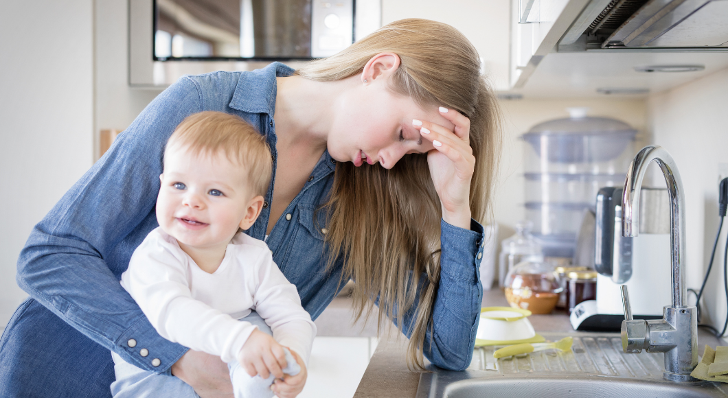 A tired mom leans on a countertop with her baby boy.