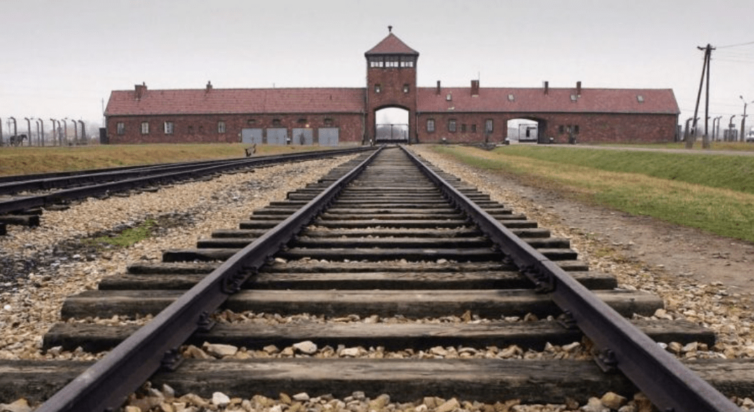 A building from the Holocaust remains with railroad tracks leading up to it. 