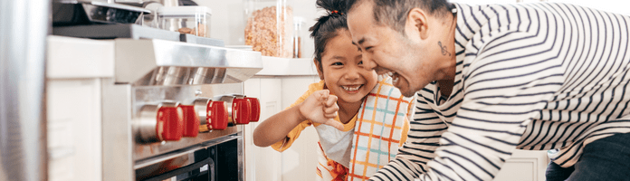 father and young daughter laughing while pulling something out of the oven