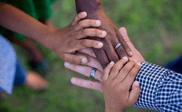 A family of mixed skin tones holds hands.