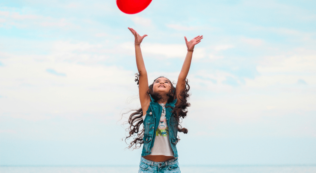 A young girl tosses a red frisbee in the air.