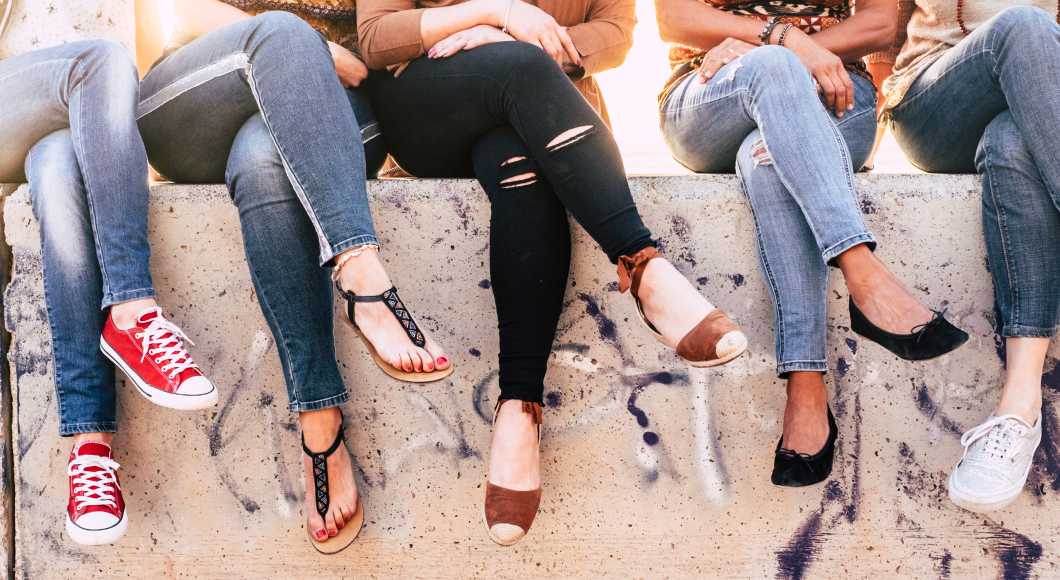 Several women sit on a wall with their legs crossed.