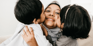 Kids kiss their mama who is wearing a head covering.