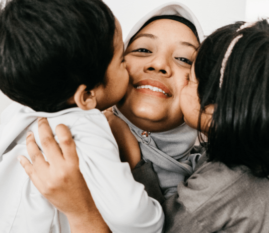 Kids kiss their mama who is wearing a head covering.