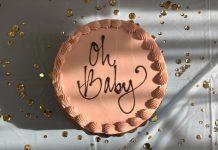 circular terracotta colored cake with 'oh baby' written on it