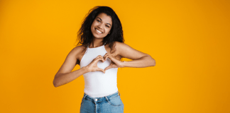 A smiling woman makes a heart shape with her hands on her chest.