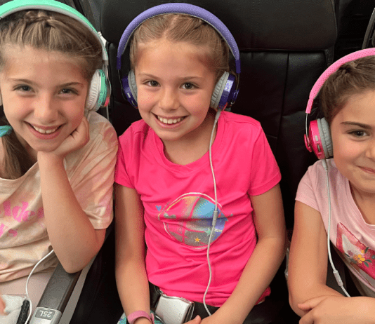 Three girls sitting on an airplane with headphones on.