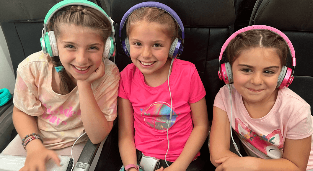 Three girls sitting on an airplane with headphones on.