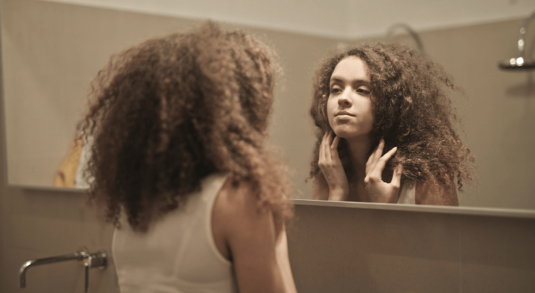 A woman looks in the mirror and touches her hair