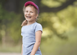 A girl in a baseball cap smiles outside.