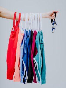 rainbow of one pieces bathing suits dangle from a woman's arm