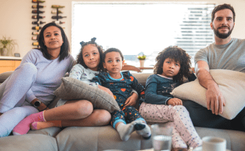 A family lounges on the couch at home in comfortable clothes.