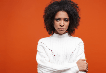 Black women wears a white sweater in front of an orange background
