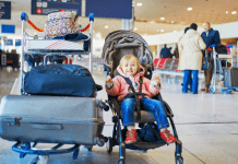 A toddler sits in a stroller with a bunch of luggage next to her.
