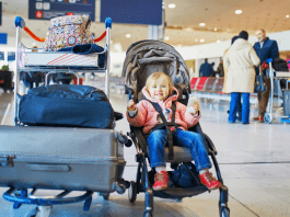 A toddler sits in a stroller with a bunch of luggage next to her.