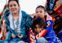 A Native American family sits close together with traditional blankets and jewelry on.