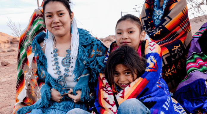 A Native American family sits close together with traditional blankets and jewelry on.