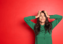 A woman puts her hands on her hand in a green shirt in front of a red background