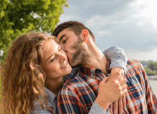 Man kisses woman on the cheek at a park on a sunny day