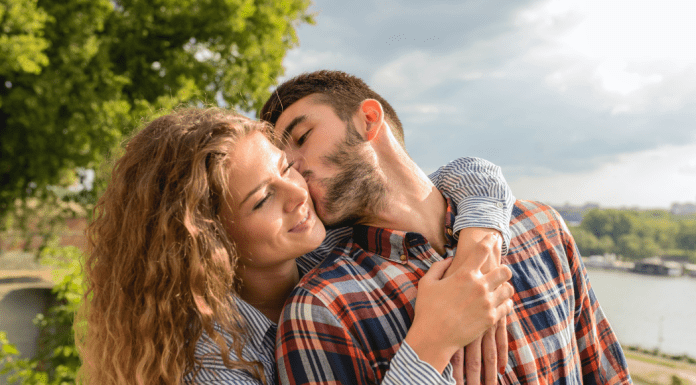 Man kisses woman on the cheek at a park on a sunny day