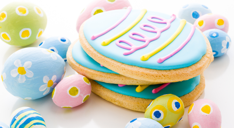 cookies shaped and decorated like Easter eggs stacked on top of one another, surrounded by small, decorated easter eggs