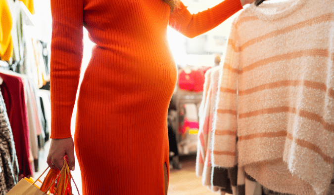Pregnant woman in a bright orange sweater dress shops for maternity clothes.