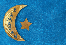 A paper plate cut into the shape of a crescent moon, painted gold, with a golden star tied to it, reads "Ramadan."
