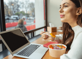 A woman eats a salad while working remotely at a restaurant.