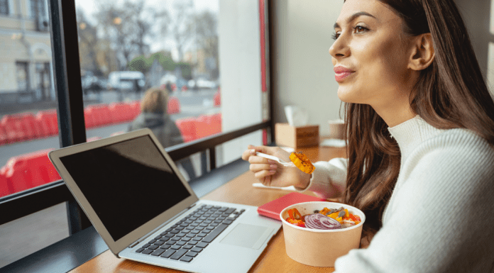 A woman eats a salad while working remotely at a restaurant.