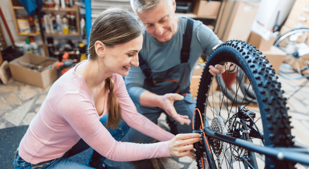 A male staff member teaches mom how to fix a chain in a bike shop.