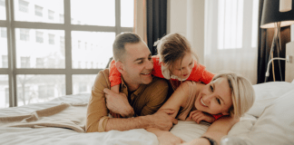 A family of three cuddle on a hotel bed on vacation.